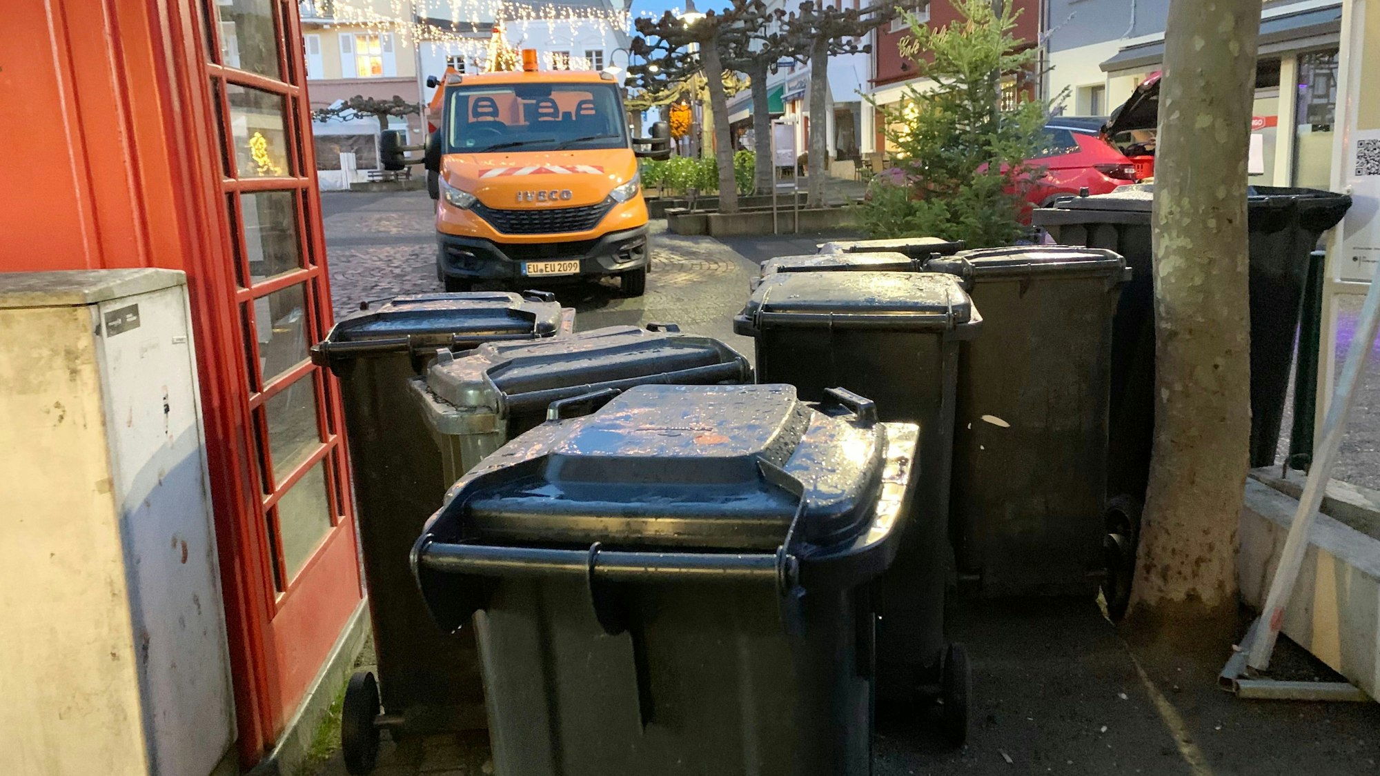 Am Rande des Alten Marktes in Euskirchen stehen graue Abfalltonnen. Im Hintergrund ein Fahrzeug der Technischen Dienste, links ein roter Bücherschrank.
