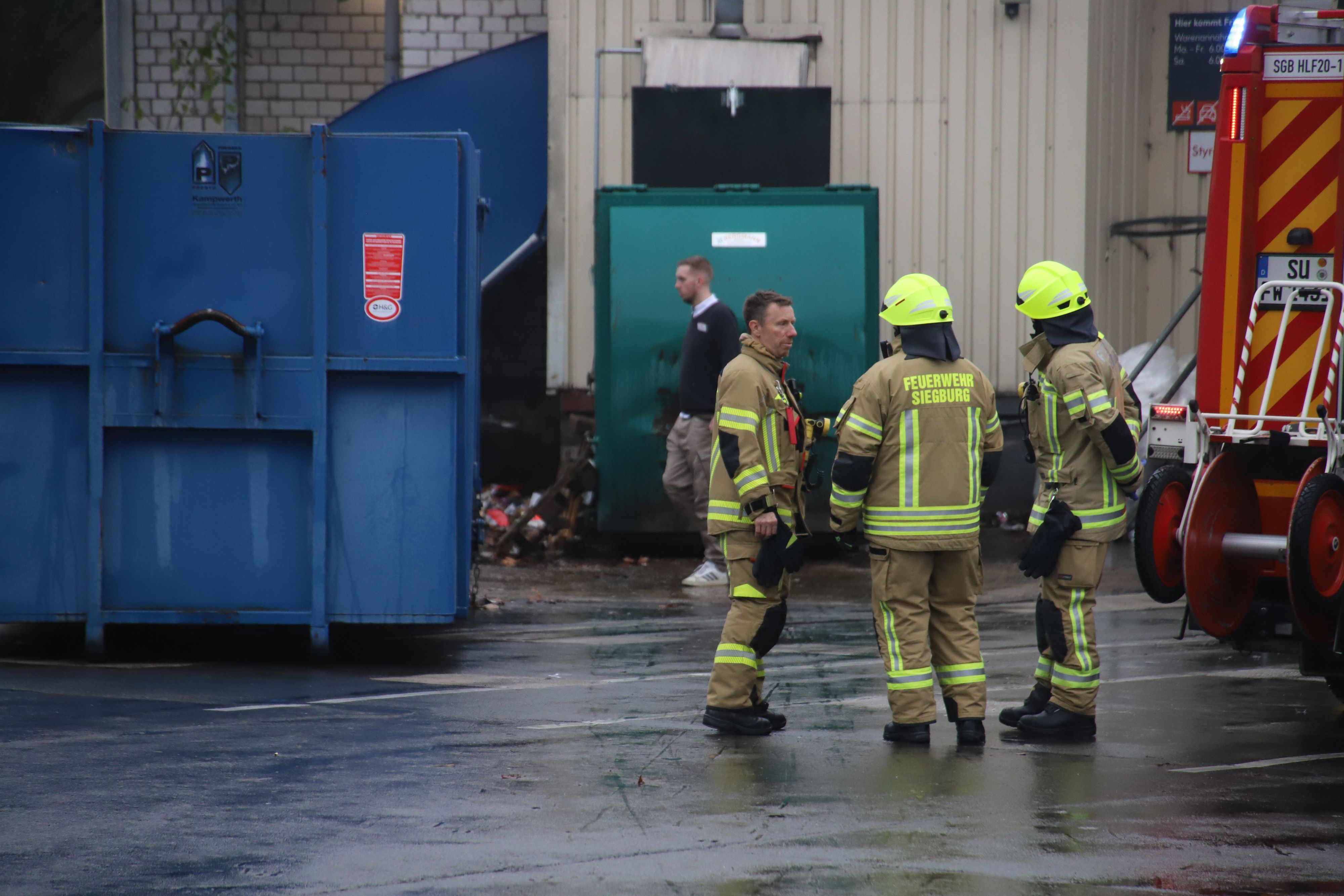 Feuerwehrleute stehen vor einer Müllpresse.