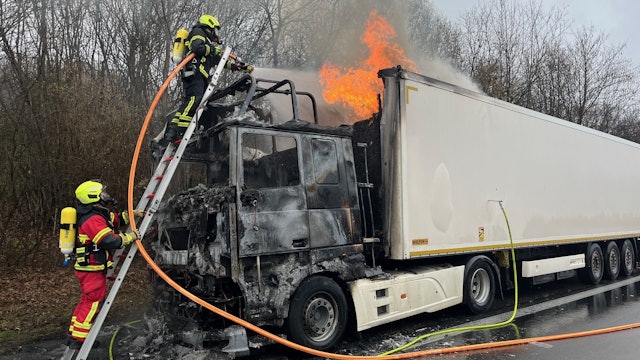 Feuerwehrleute unter Atemschutz löschen mit einer Leiter.