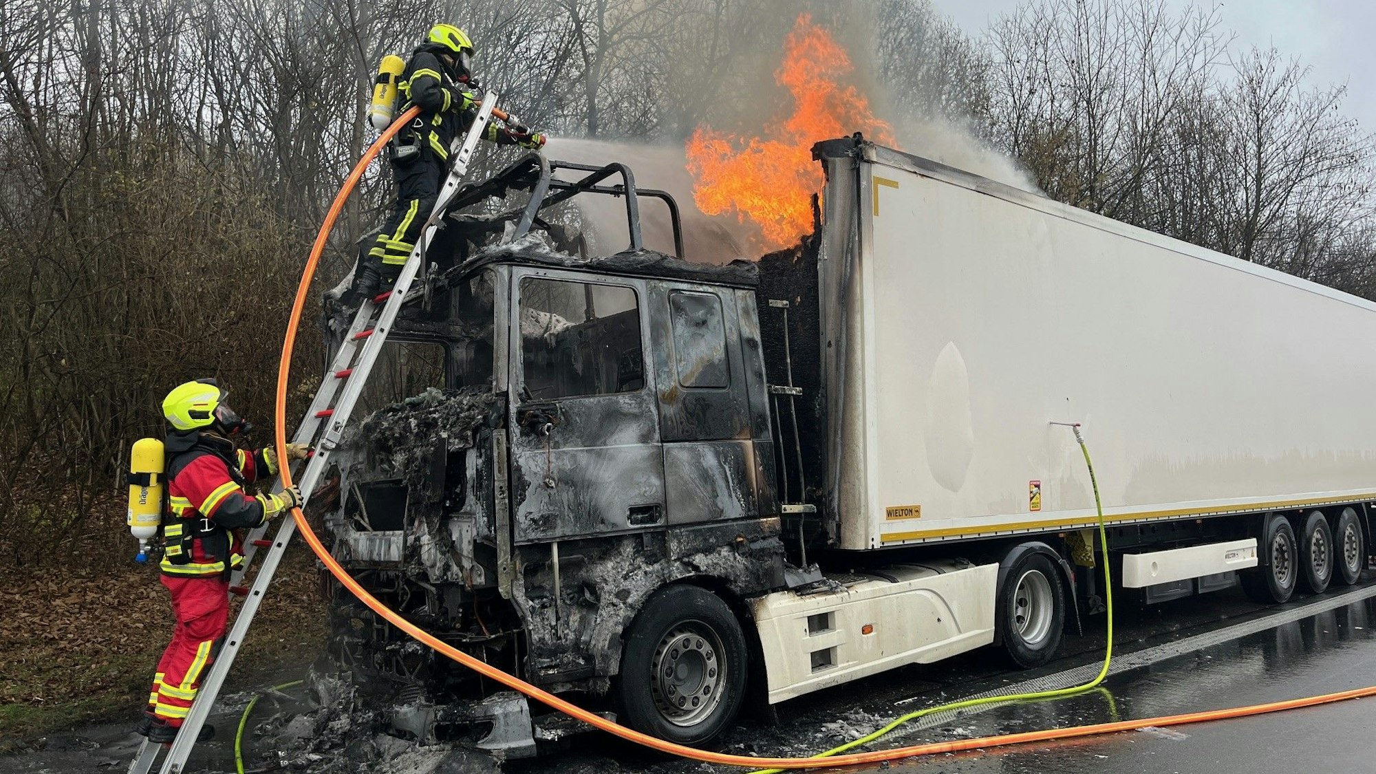 Feuerwehrleute unter Atemschutz löschen mit einer Leiter.