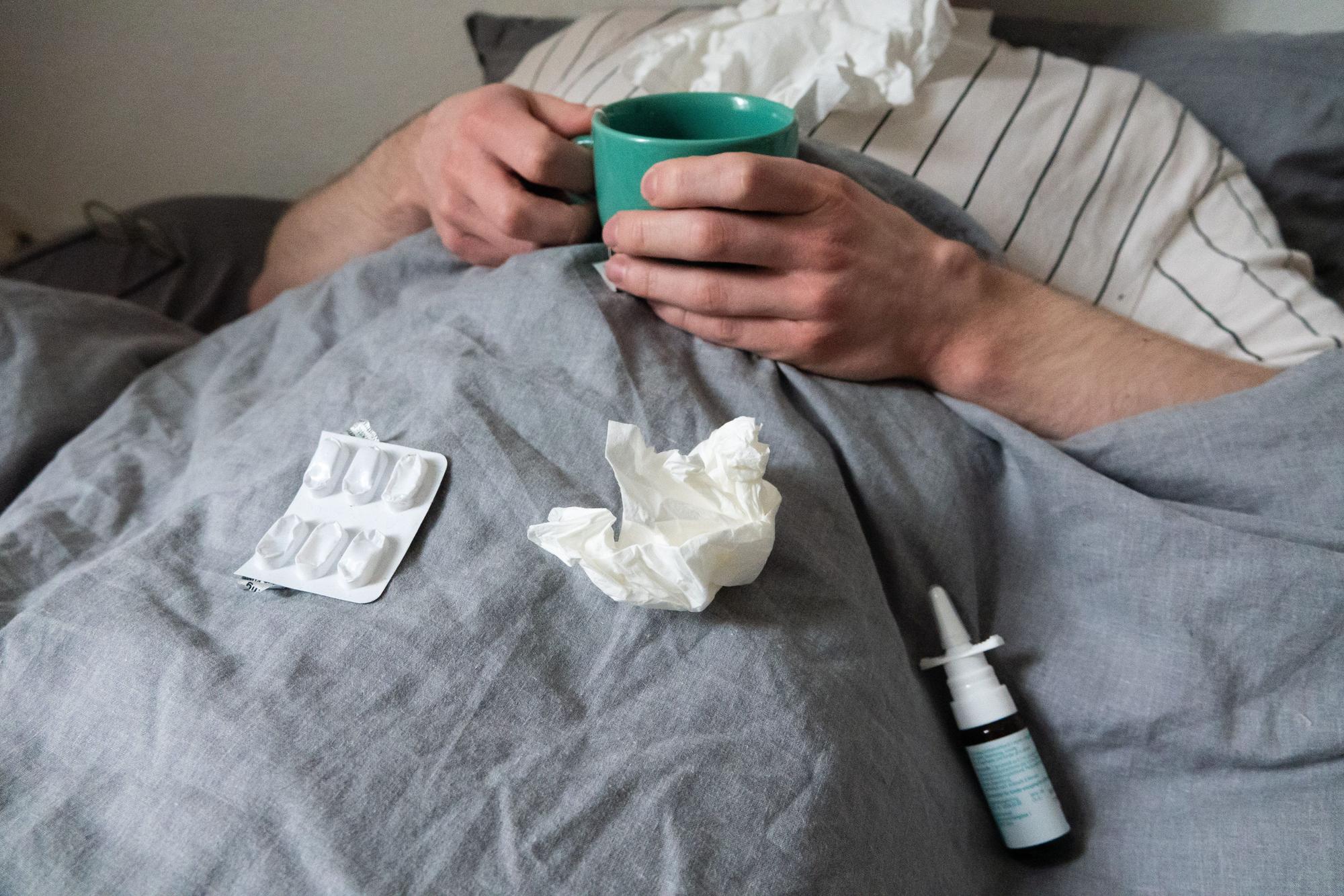 12.12.2023, Niedersachsen, Hannover: ILLUSTRATION - Ein Mann liegt mit Taschentüchern, Teetasse, Nasenspray und Tabletten im Bett (gestellte Szene). Derzeit bewegt sich die Rate akuter Atemwegserkrankungen in der Bevölkerung weiter auf einem relativ hohen Niveau im Vergleich zu früheren Jahren. Foto: Philip Dulian/dpa +++ dpa-Bildfunk +++