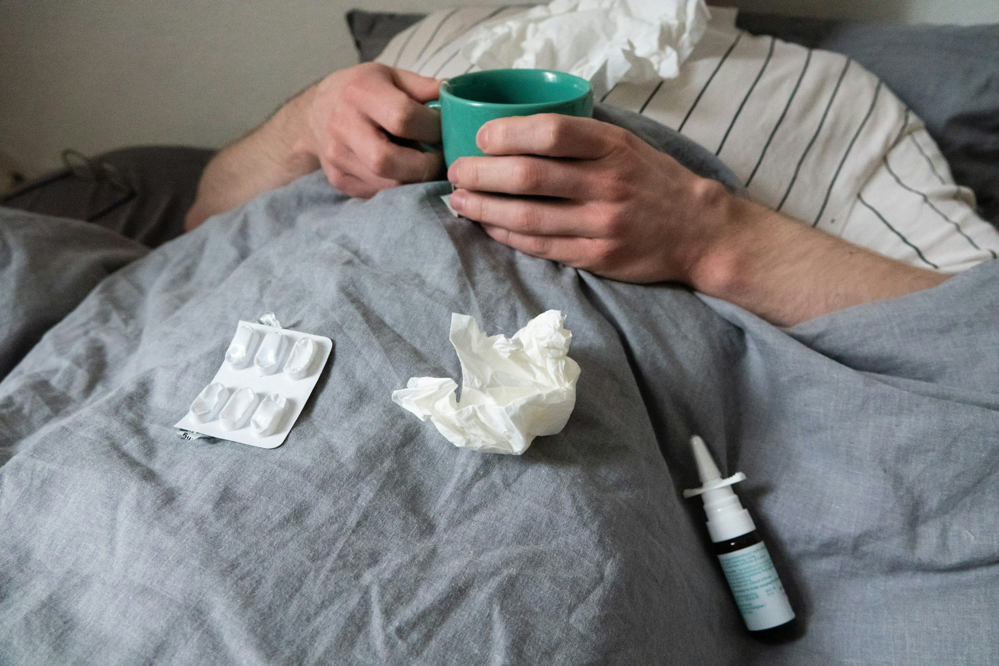 12.12.2023, Niedersachsen, Hannover: ILLUSTRATION - Ein Mann liegt mit Taschentüchern, Teetasse, Nasenspray und Tabletten im Bett (gestellte Szene). Derzeit bewegt sich die Rate akuter Atemwegserkrankungen in der Bevölkerung weiter auf einem relativ hohen Niveau im Vergleich zu früheren Jahren. Foto: Philip Dulian/dpa +++ dpa-Bildfunk +++