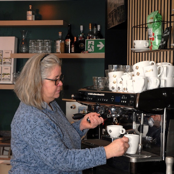 Eine Frau steht an einer Kaffeemaschine.