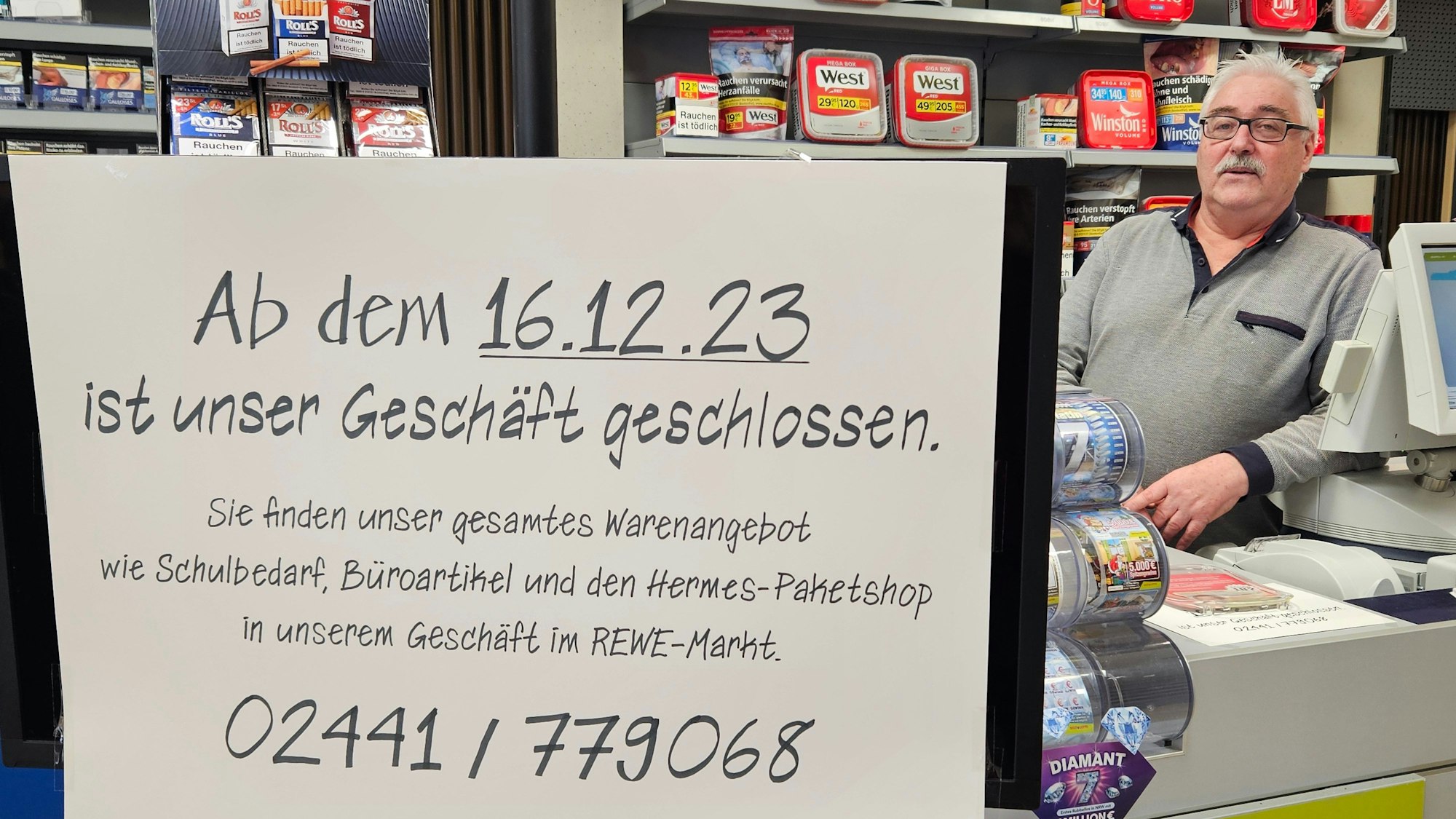 Hans-Dieter Pütz steht hinter einem Schild, das die Schließung des Geschäfts ankündigt, am Tresen.
