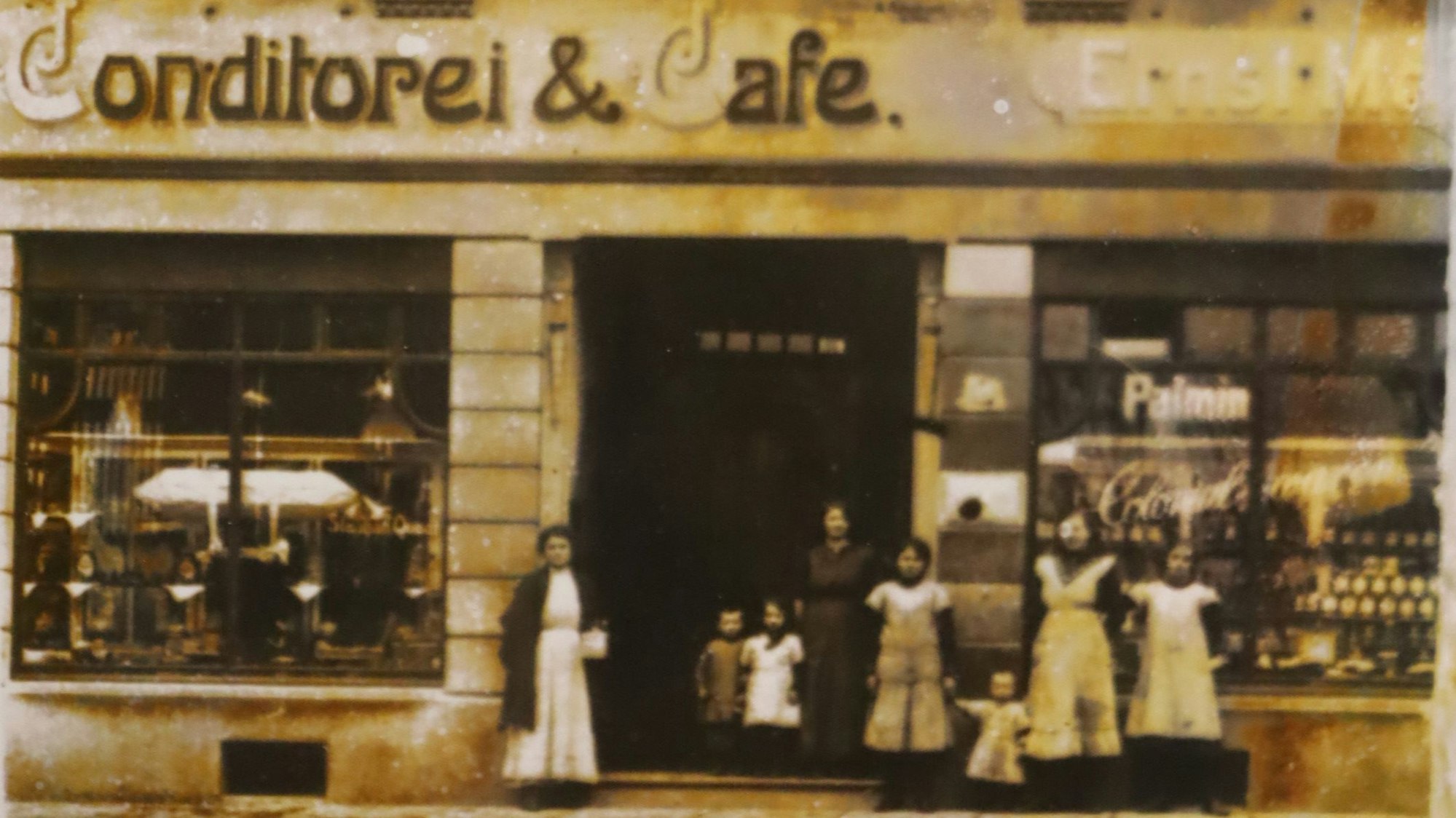 Das vergilbte Schwarz-Weiß-Bild zeigt eine historische Aufnahme eines Ladenlokals mit Frauen in Schützen und Kindern.