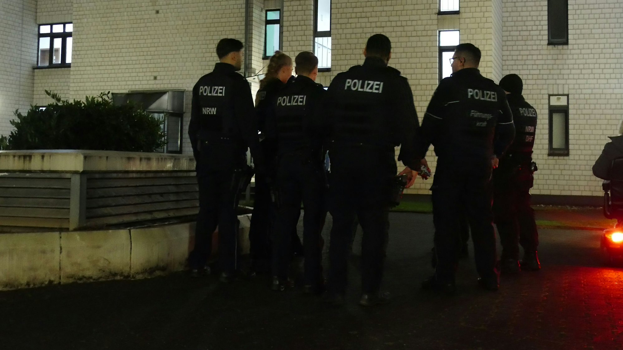 Eine Gruppe Polizeibeamte stehen mit dem Rücken zur Kamera vor dem Haus, in dem der Tote gefunden wurde.