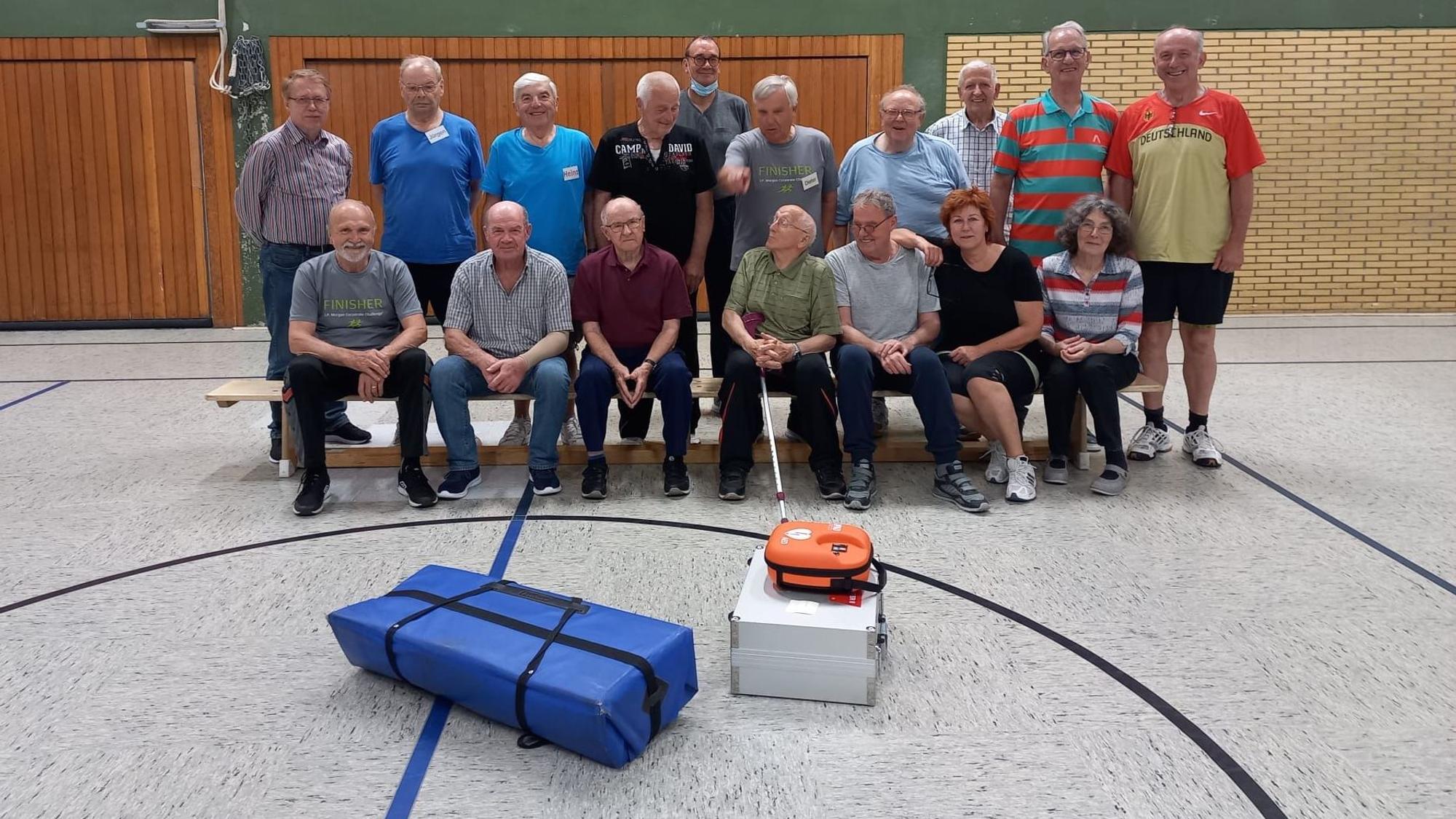 Ein Gruppe Männer und Frauen sitzt und steht in einer Sporthalle.