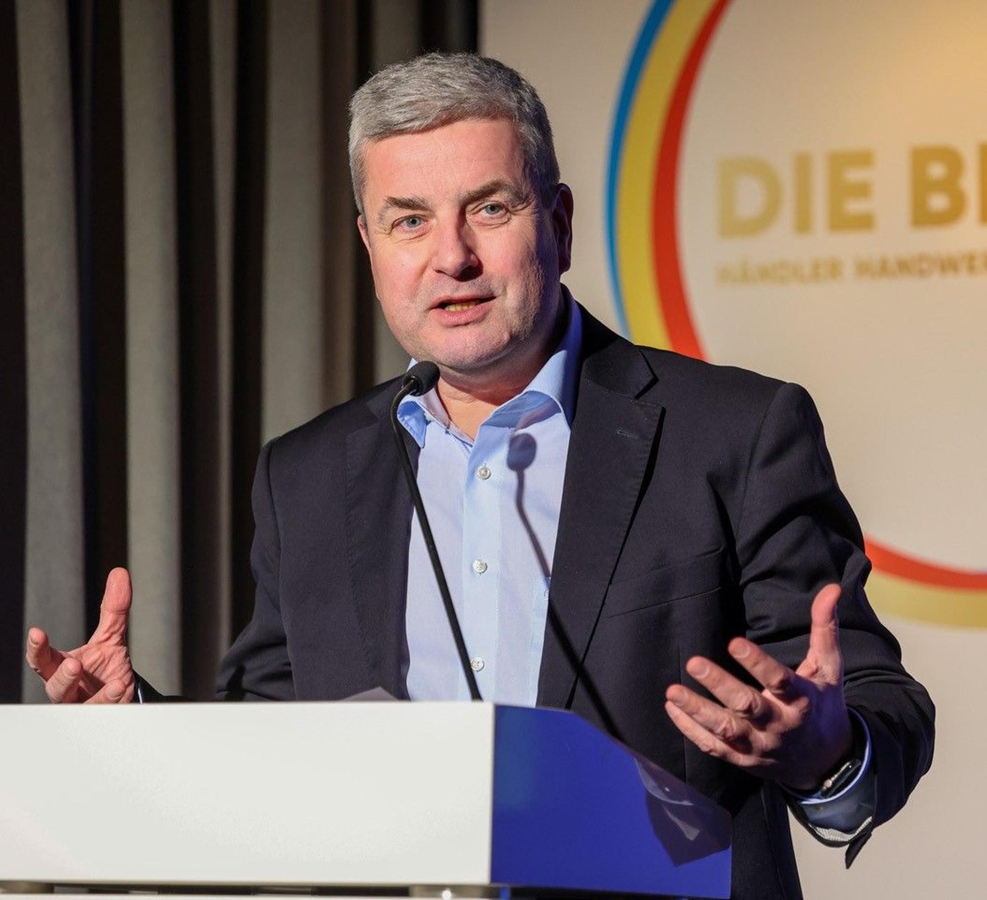Auf dem Bild ist das Portrait eines Mannes an einem Rednerpult zu sehen.