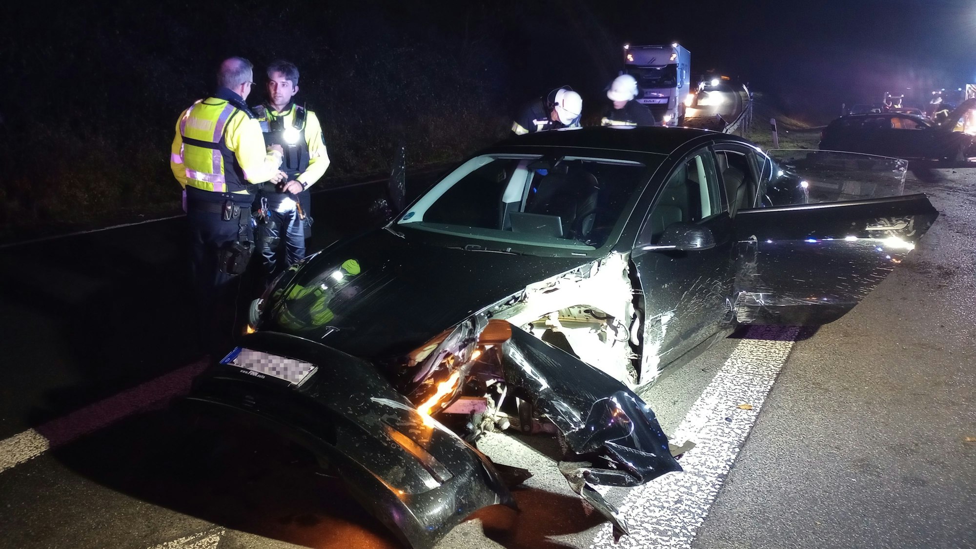 Polizisten und Feuerwehrleute neben einem beschädigten Tesla.