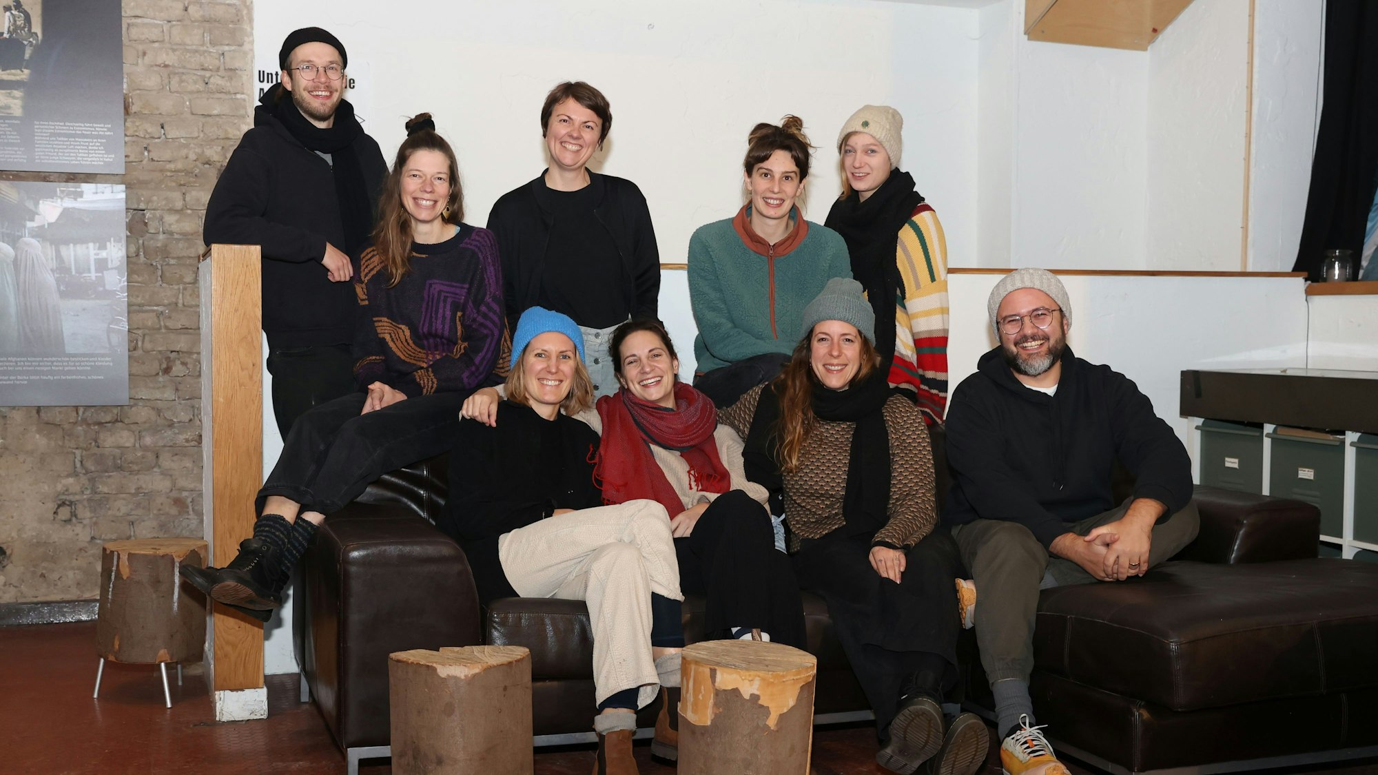 Sieben Frauen und Männer sitzen auf einem Ledersofa oder stehen dahinter.