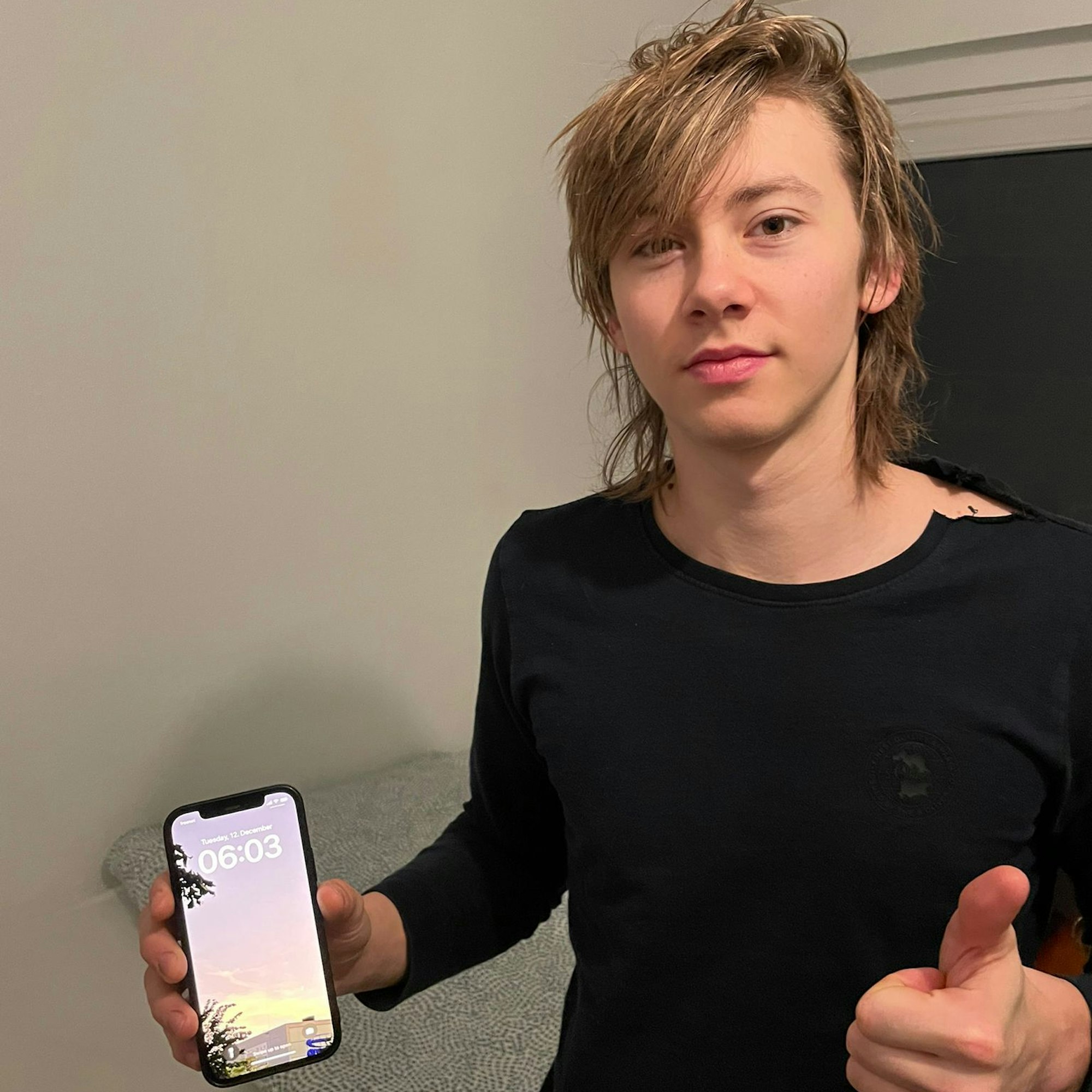 Ein junger Mann hält verschlagen einen Handywecker in der Hand, der 6 Uhr anzeigt.