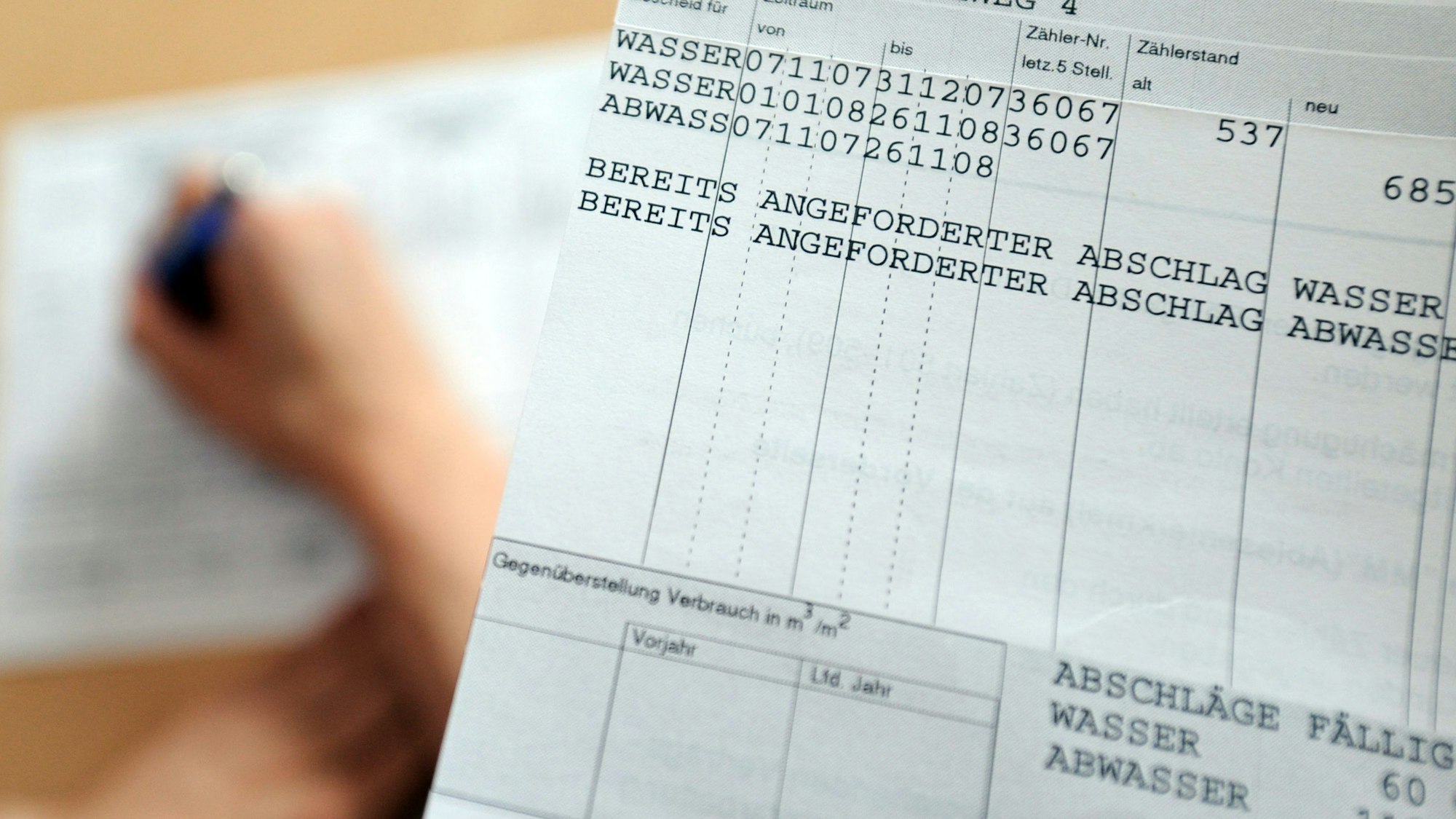 Blick auf einen Abwassergebührenbescheid, im Hintergrund füllt jemand einen Fragebogen zur neu Berechnung der Abwassergebühr aus.