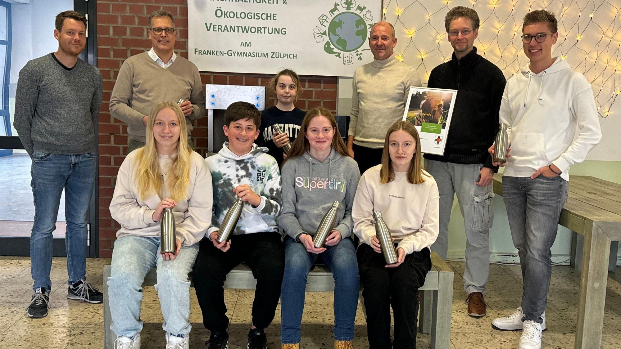 Schülerinnen und Schüler des Franken-Gymnasiums sitzen auf einer Bank und haben Trinkflaschen in den Händen. Links und rechts neben ihnen stehen Lehrer, der Bürgermeister und ein Vertreter der Westenergie.