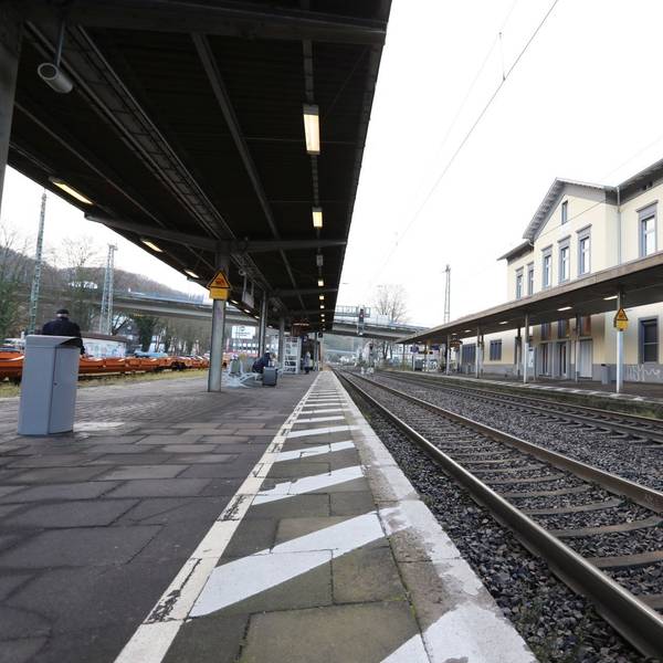 Zwischen einem überdachten Bahnsteig und dem Bahnhofsgebäude verlaufen die Gleise der rechtsrheinischen Bahntrasse.