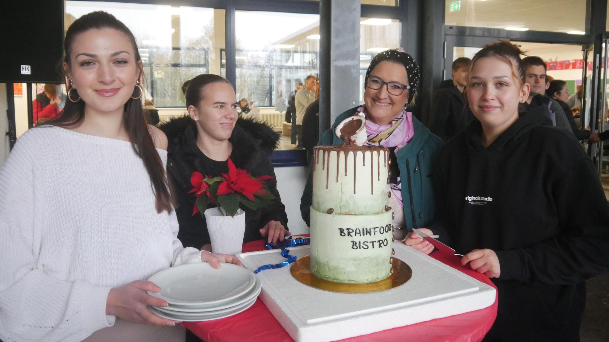Drei Schülerinnen und eine Lehrerin stehen neben einer mehrstöckigen Torte zum Jubiläum.