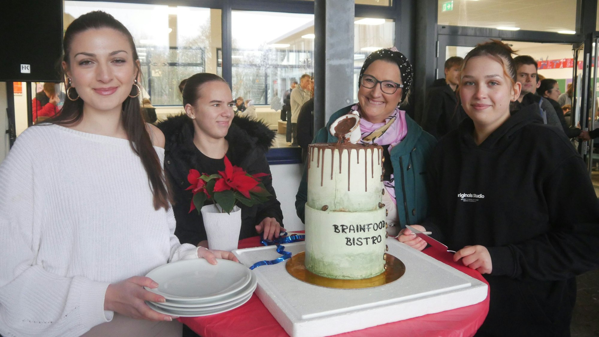 Drei Schülerinnen und eine Lehrerin stehen neben einer mehrstöckigen Torte zum Jubiläum.