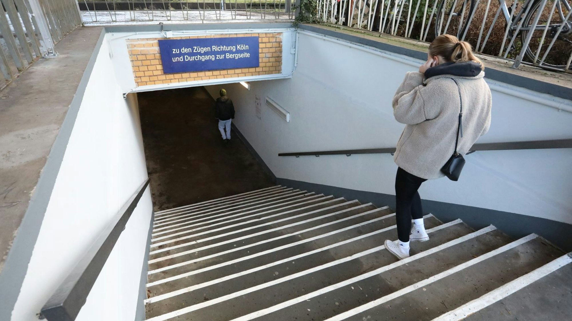 Eine Frau steigt mit dem Handy telefonierend eine Treppe herunter zur Fußgängerunterführung.