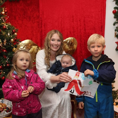 Zwei Kinder stehen um das Christkind von Engelskirchen herum. Das Christkind hat ein Kleinkind auf dem Schoß, sie überreichen bunt gestaltete Wunschzettel.