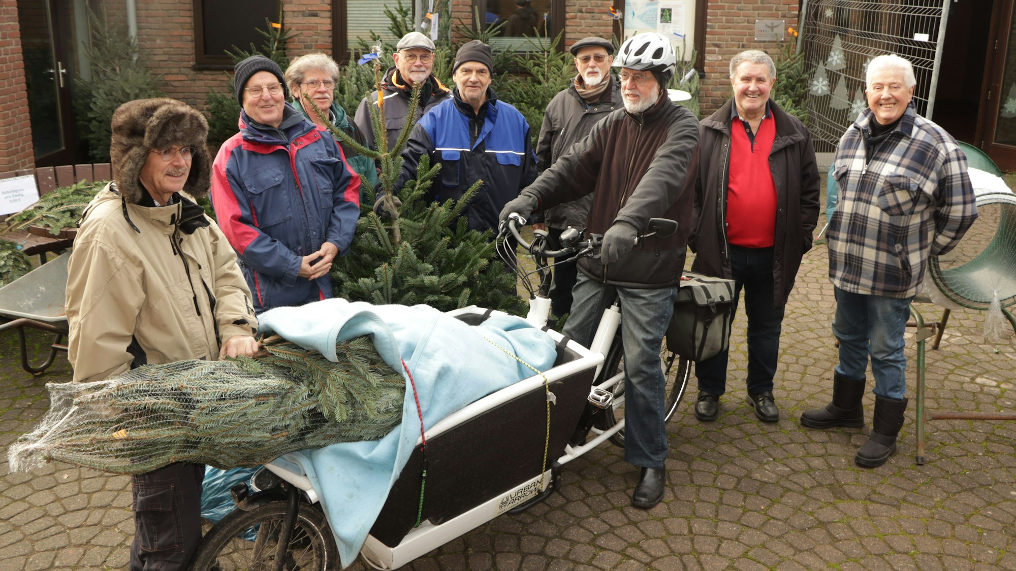 Eine Gruppe von Männern mit Tannenbäumen. Im Vordergrund ein Weihnachtsbaum auf einem Lastenrad.