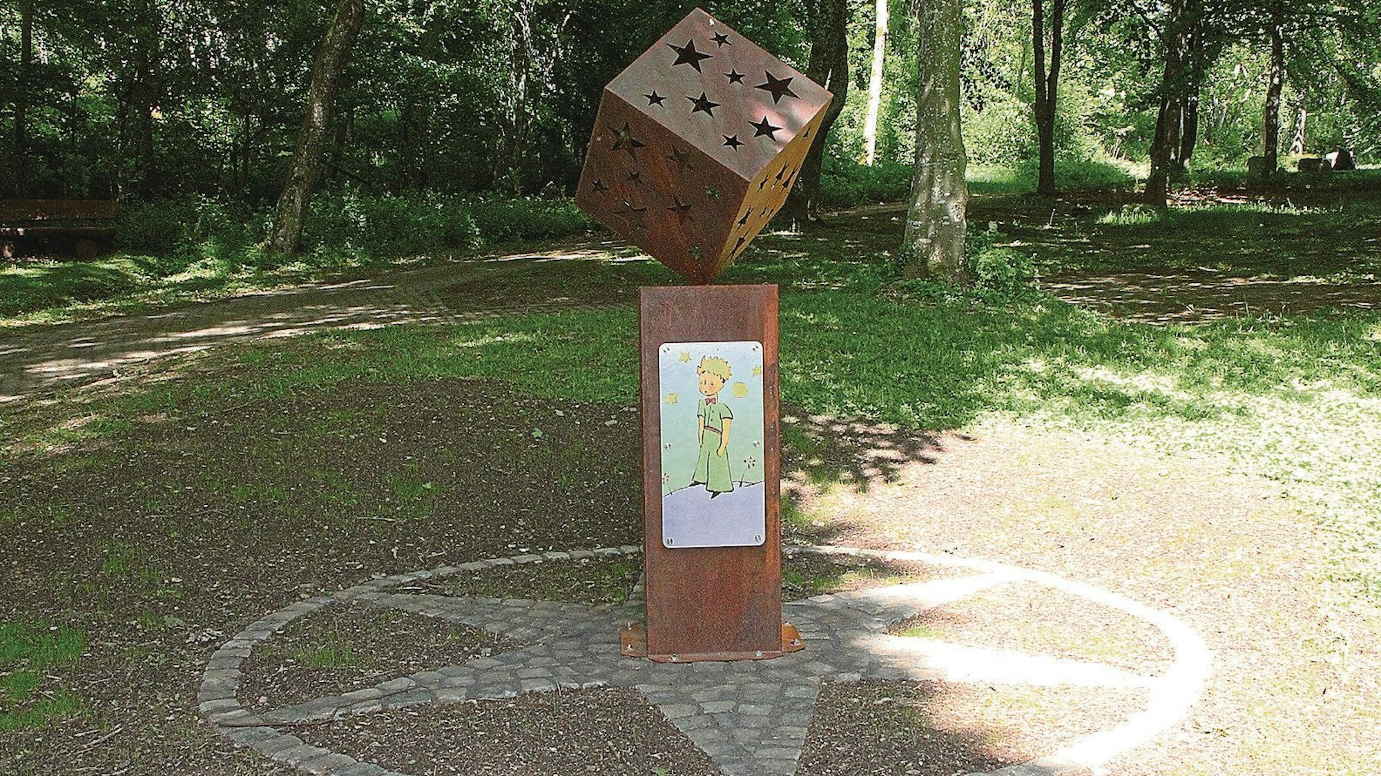 Auf dem Friedhof in Blankenheim steht eine Stele auf einer Rasenfläche. Darauf ist ein Abbild des kleinen Prinzen.