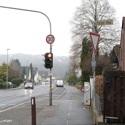 An einer Fußgängerampel auf der Altenberger-Dom-Straße ist ein Tempo 30-Verkehrsschild angebracht. Eine Fußgängerin überquert die Straße.