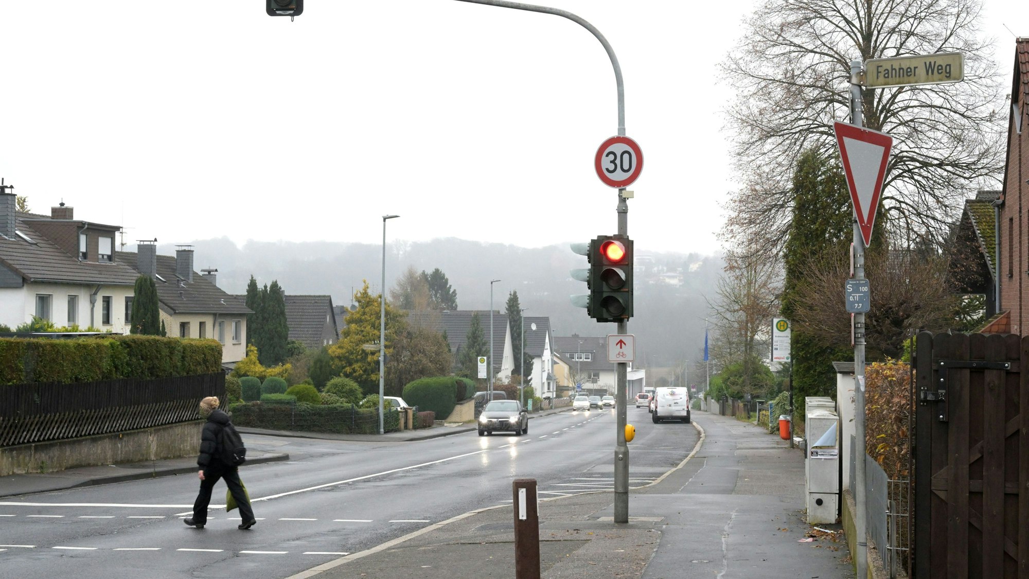 An einer Fußgängerampel auf der Altenberger-Dom-Straße ist ein Tempo 30-Verkehrsschild angebracht. Eine Fußgängerin überquert die Straße.