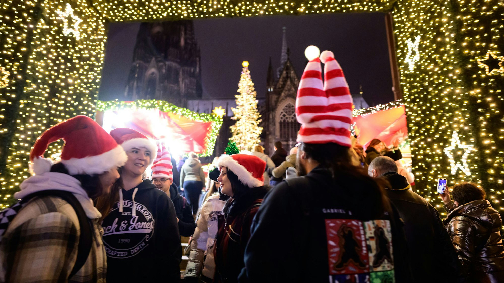 Junge Menschen mit Weihnachtsmützen stehen unter einem Lichterbogen.