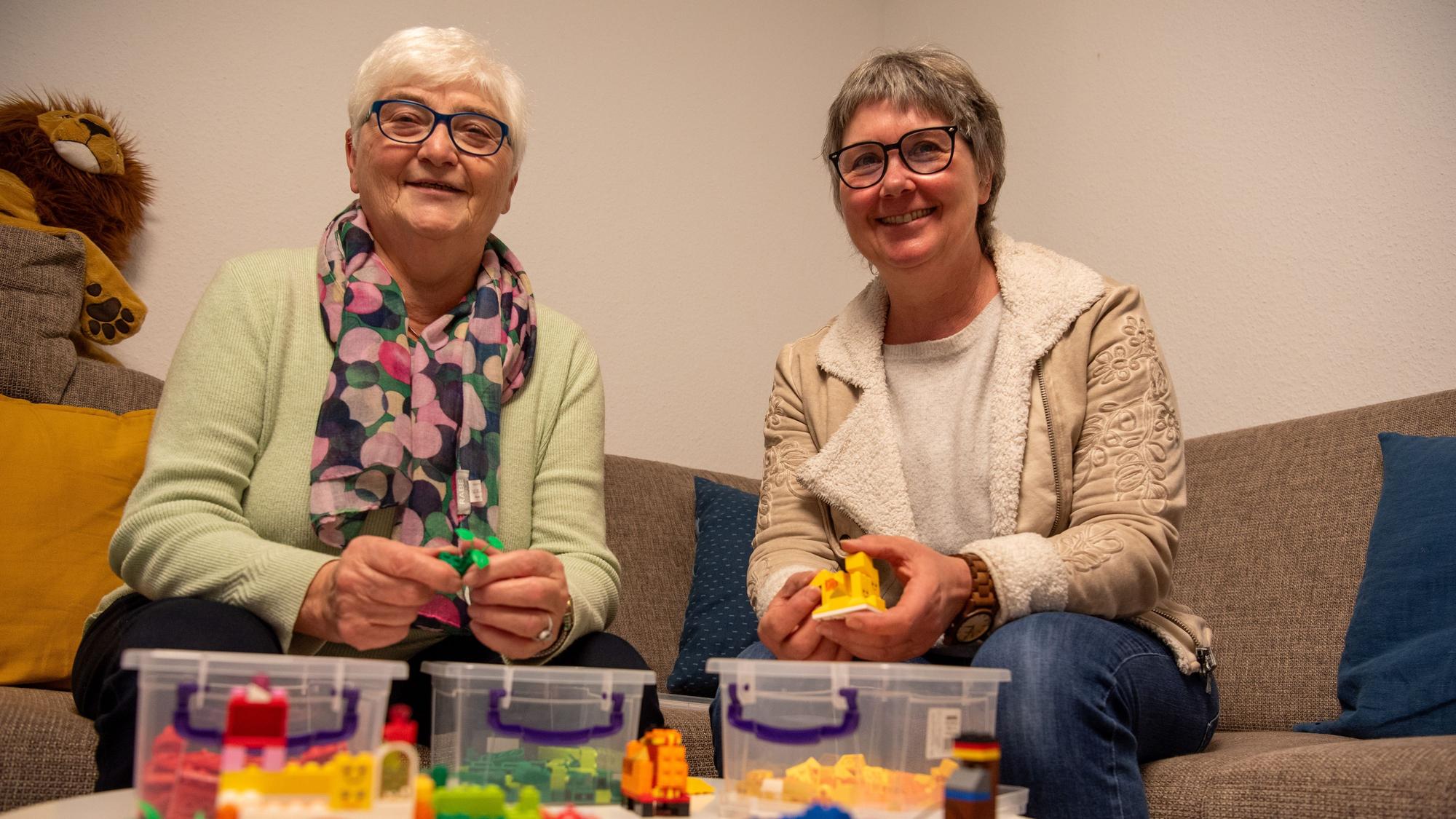Das Bild zeigt Anita Sauer (l.) und Vera Schröder auf einem Sofa sitzend. Vor ihnen steht auf einem Tisch Lego-Spielzeug.