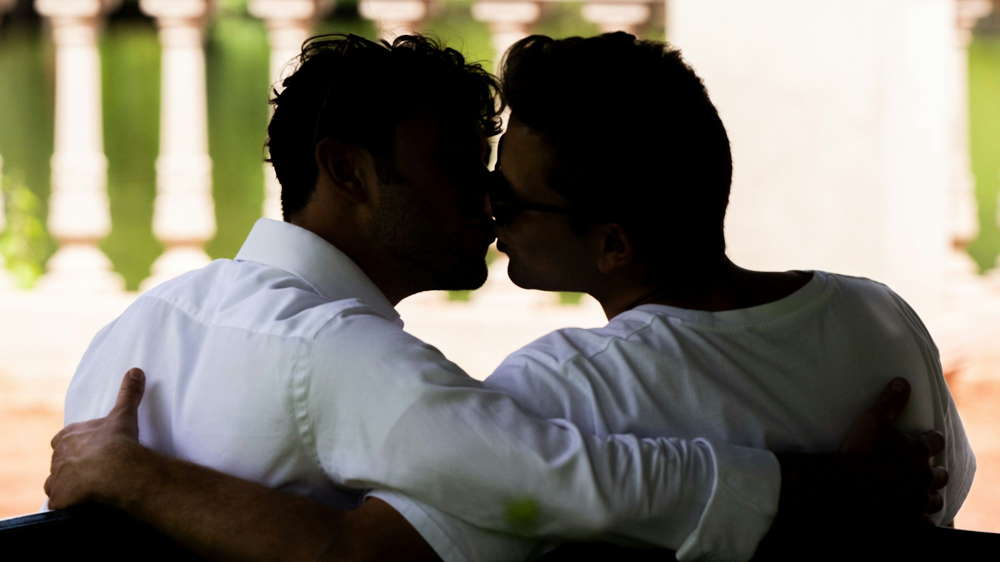 Zwei Männer sitzen auf einer Bank und küssen sich.