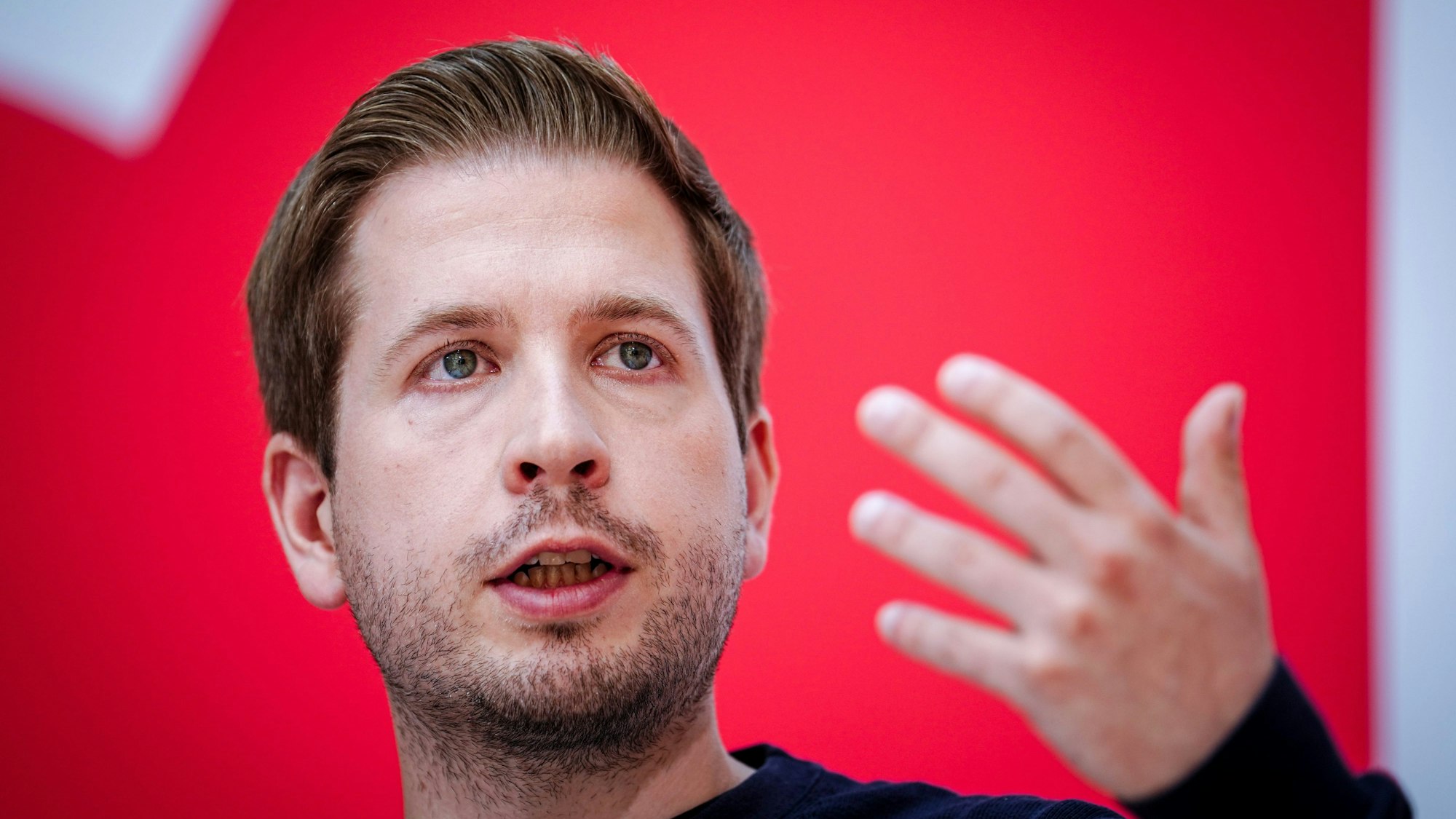 Nahaufnahme von Kevin Kühnert, SPD-Generalsekretär, vor einem roten Hintergrund, während er eine Hand erhebt, die unscharf gestellt wurde. (Archivbild)