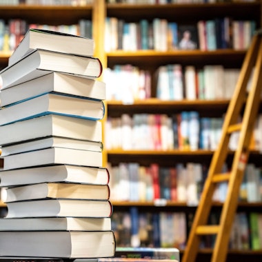 Ein Bücherstapel steht vor einem Bücherregal.