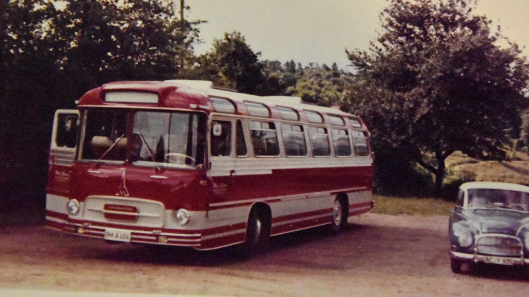 Ein roter Bus steht neben einem Auto.