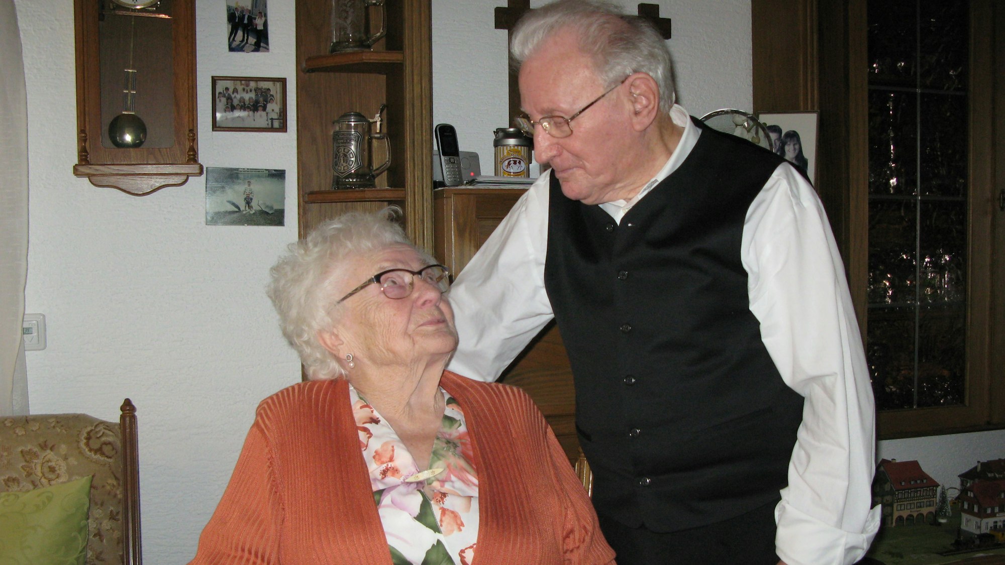 Das Gnadenhochzeitspaar Heinz und Trudel Wett schaut sich an. Er steht, sie sitzt auf einem Stuhl im Wohnzimmer.