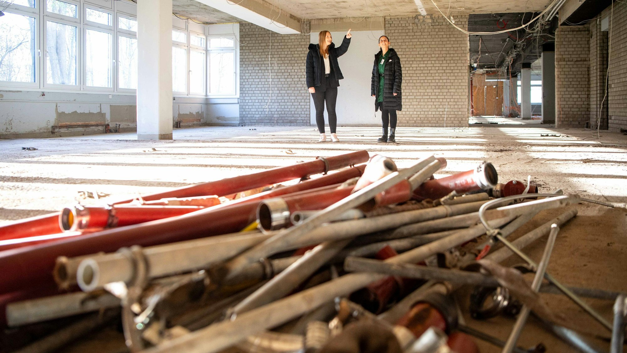 Das Bild zeigt zwei Schülerinnen in dem Rohbau. Kabel hängen von der Decke und Rohre sowie Leitungen liegen auf dem Boden.