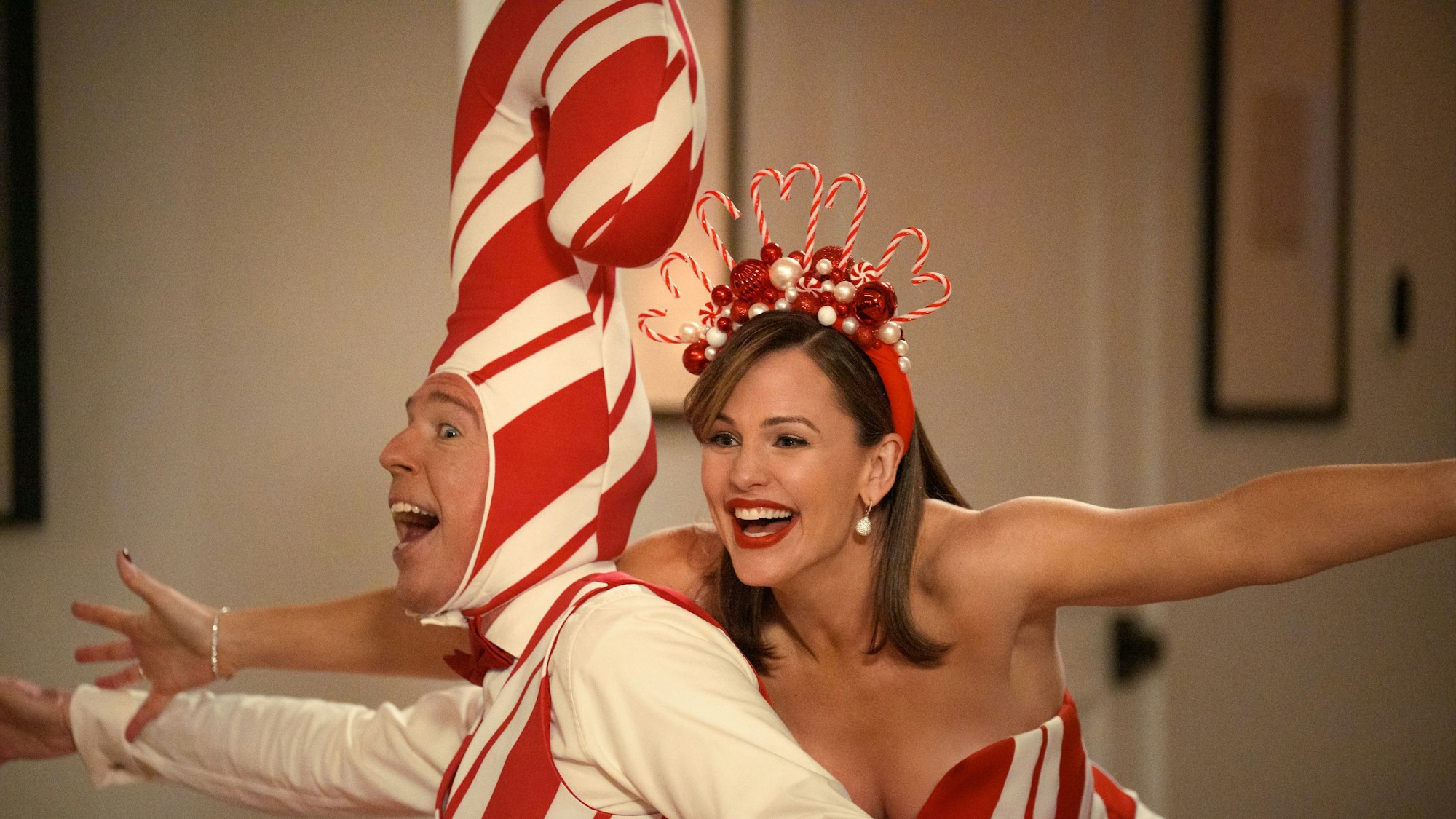 Ed Helms trägt eine Mütze in Form einer Zuckerstange. Er und Jennifer Garner halten die Arme weit auseinander.