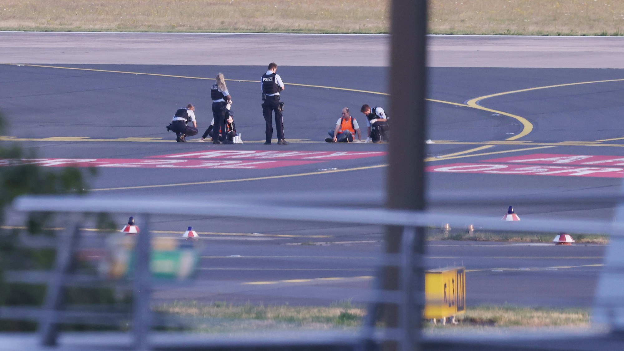 Polizistinnen und Polizisten stehen neben Mitgliedern der Klima-Gruppe Letzte Generation, die sich im Juli 2023 auf dem Rollfeld am Düsseldorfer Flughafen festgeklebt haben.