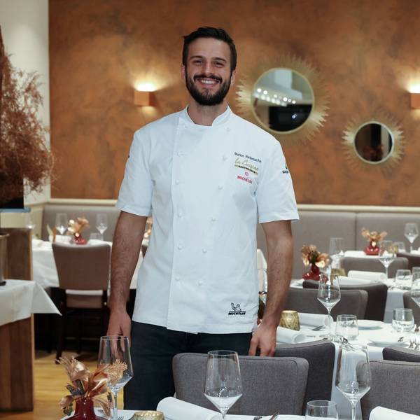 Gastronom Malon Rademacher in weißem Koch-Hemd zwischen den Tischen seines Restaurants.