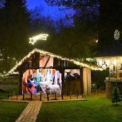 Eine lebensgroße Krippe steht in einem mit Lichterketten geschmückten Garten.