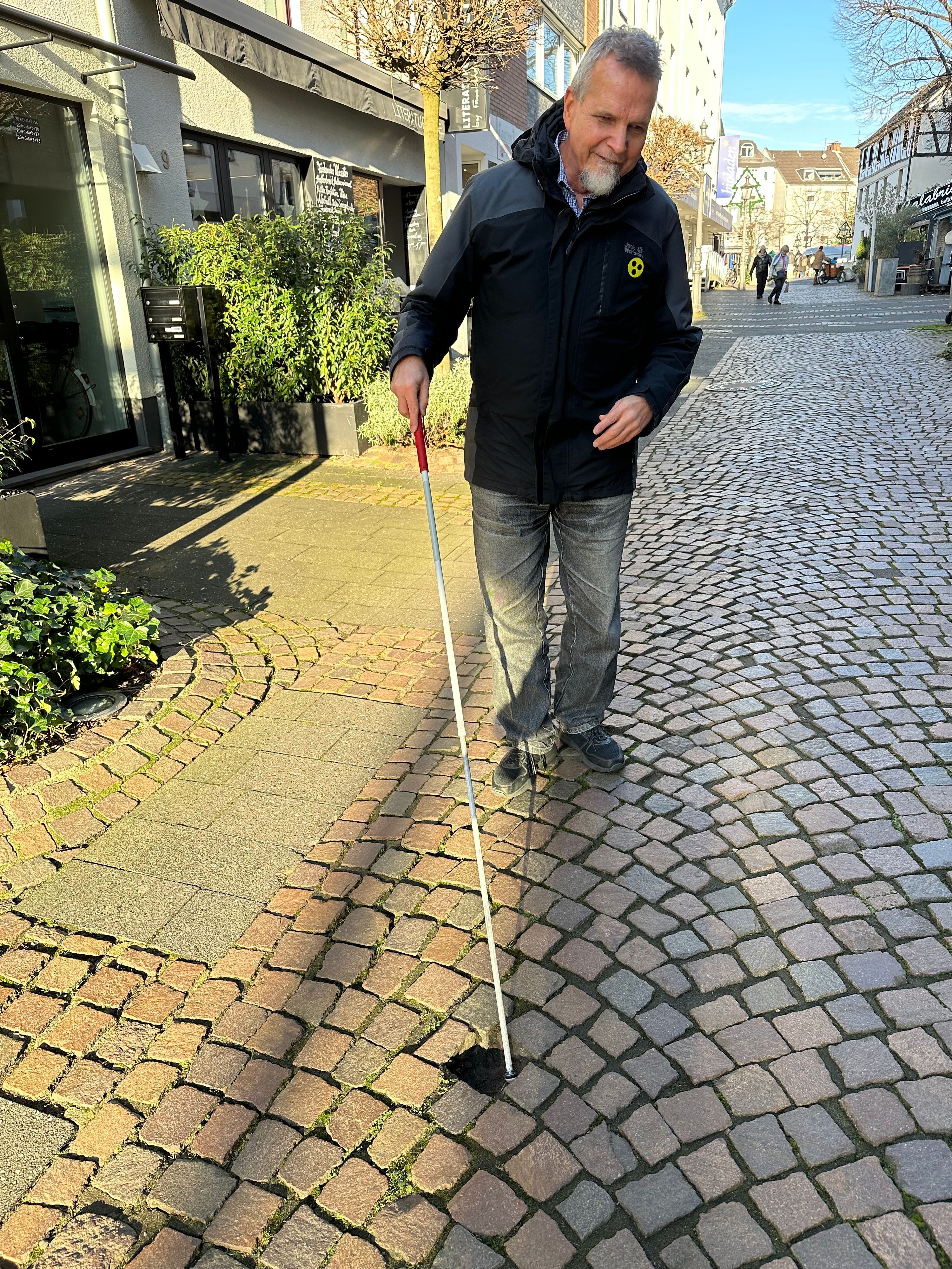 Günther Heger findet mit seinem Blindenstock ein Loch im Pflaster des Weges. Eine mögliche Stolperfalle.