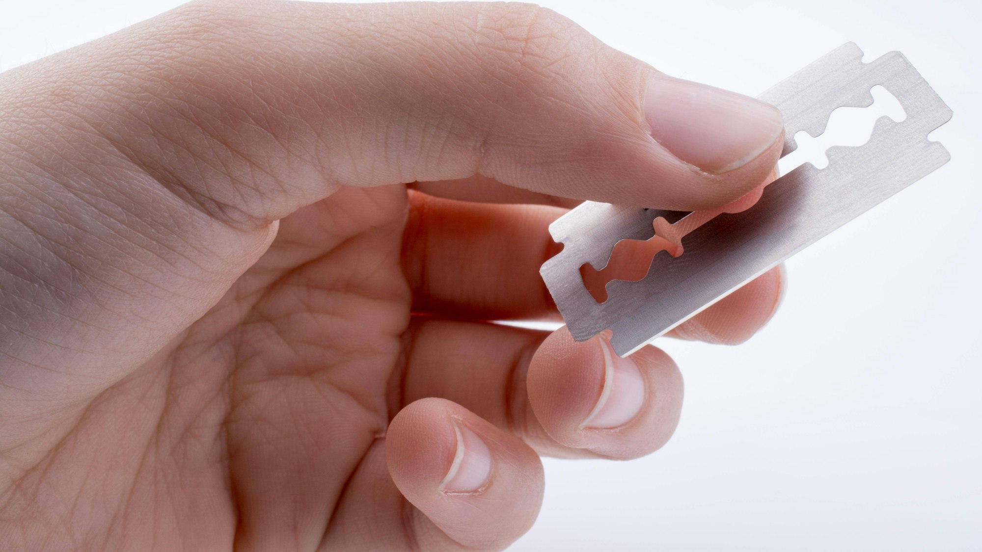 Eine Hand hält eine Rasierklinge auf weißem Hintergrund.