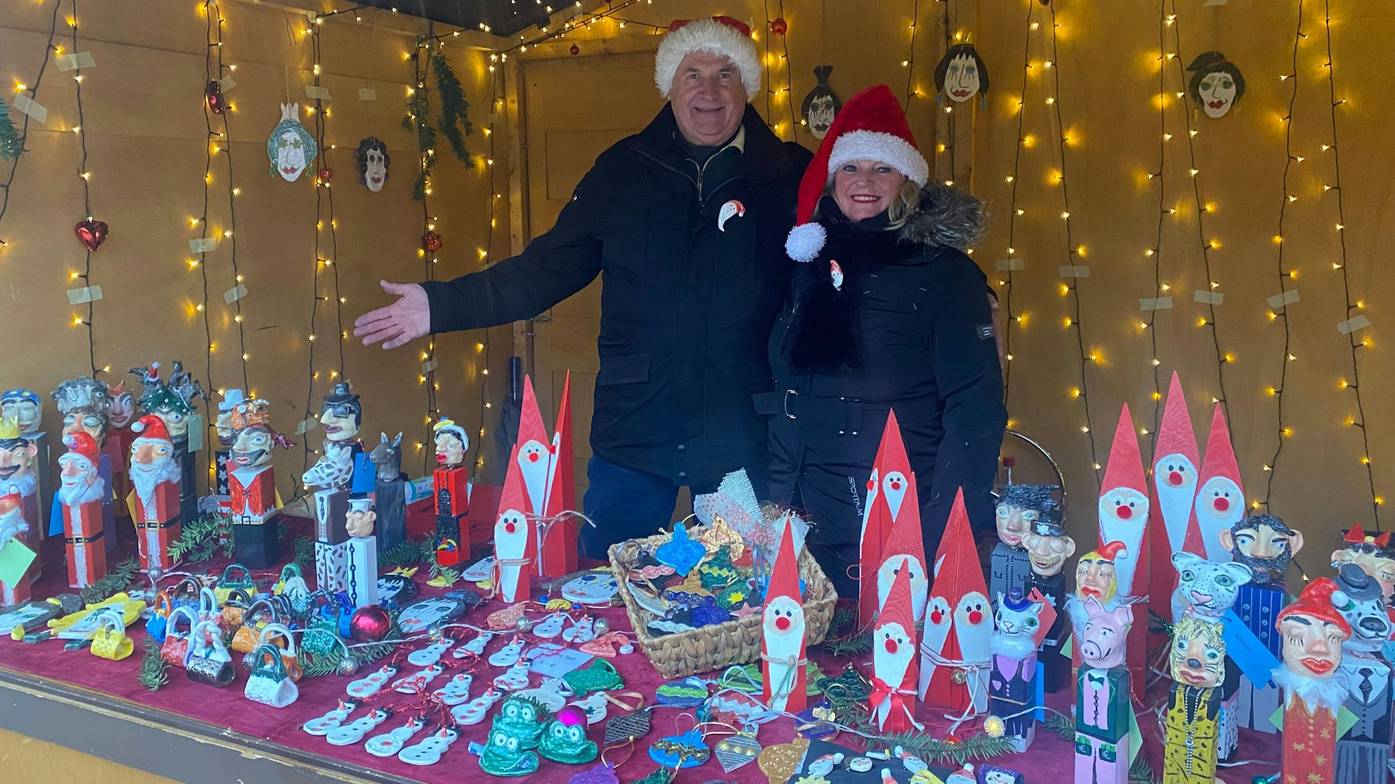 Ein Mann und eine Frau mit Weihnachtsmütze auf dem Kopf stehen an ihrem Verkaufsstand.
