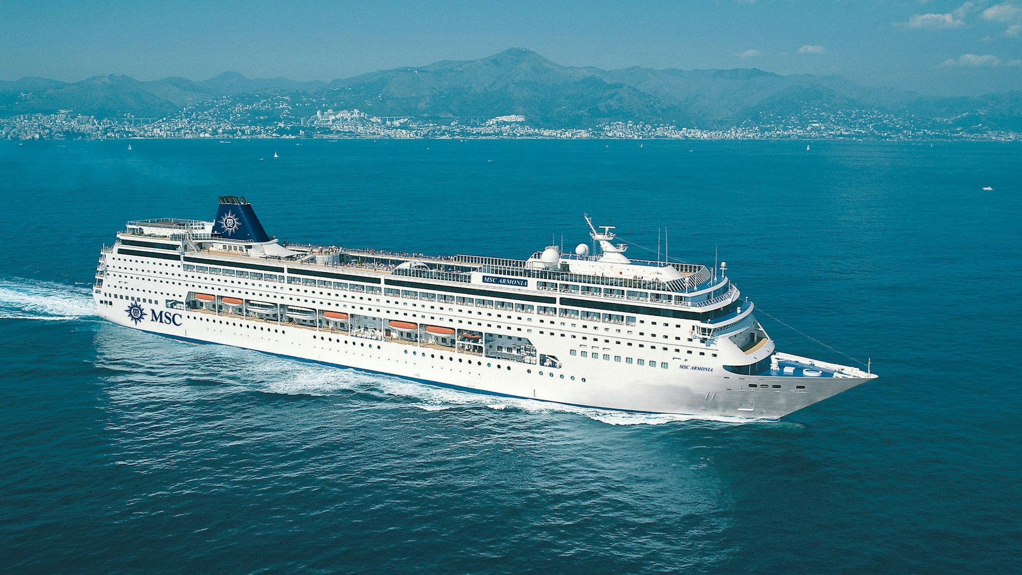 Das Kreuzfahrtschiff „MSC Armonia“ fährt vor einer Küstenstatd durch den Ozean. An Bord haben mehr als 2300 Menschen Platz.