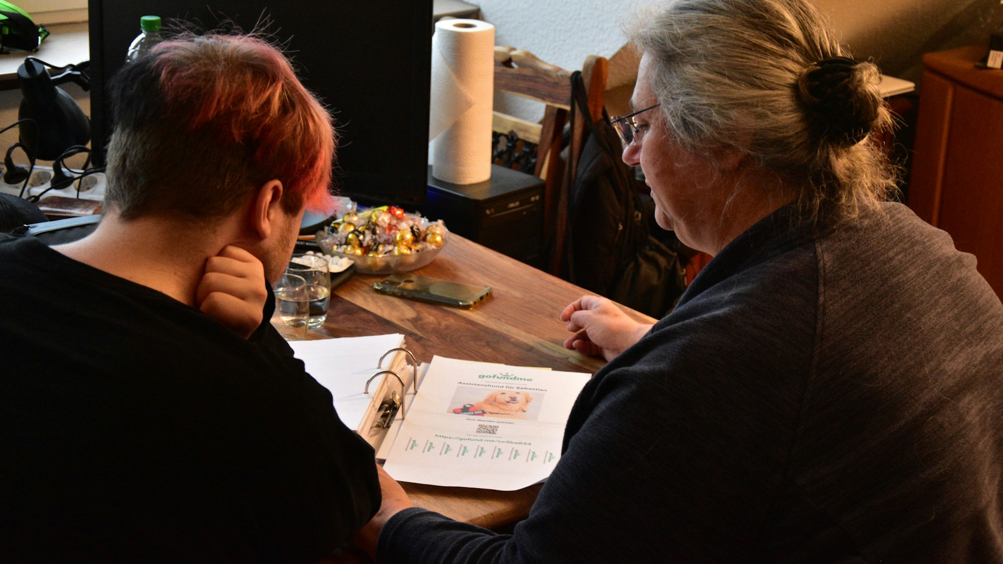 Mutter und Sohn sitzen am Tisch und gucken Unterlagen durch.