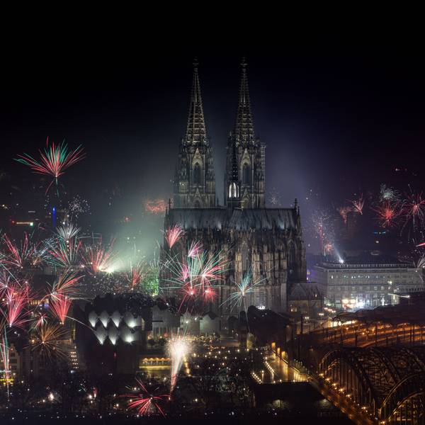 Feuerwerk explodiert zum Jahreswechsel rund um den Kölner Dom, dieser und die Hohenzollernbrücke ist angeleuchtet.