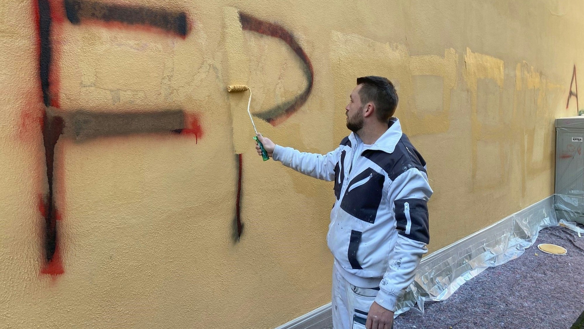 Zu sehen ist ein Maler, der Gaffiti an der Rathausfassade überstreicht.