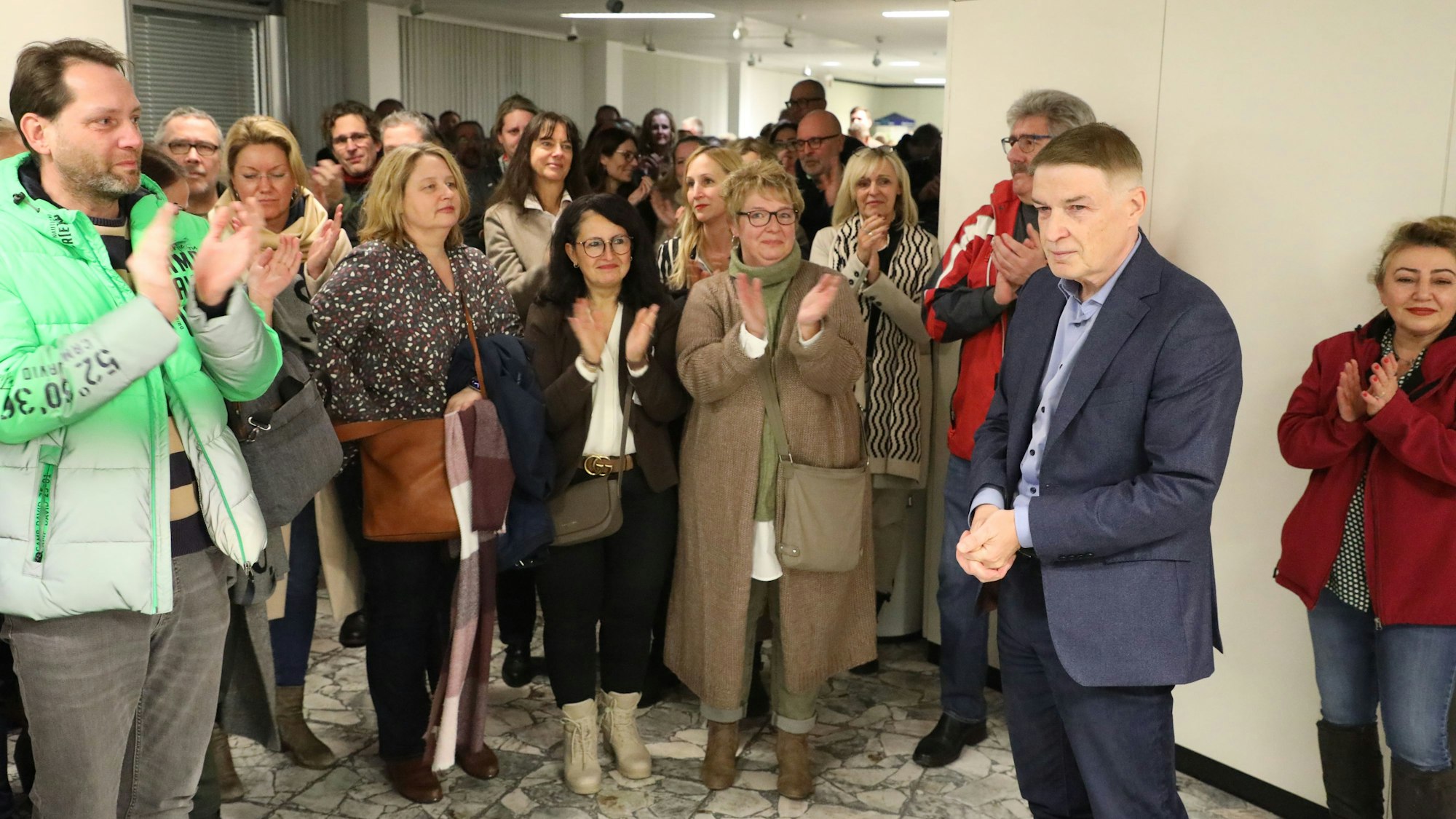 Kreisdirektor Dr. Erik Werdel steht vor der Tür des großen Sitzungssaals im Kreishaus am Rübezahlwald in Bergisch Gladbach. Mehrere Menschen applaudieren ihm
