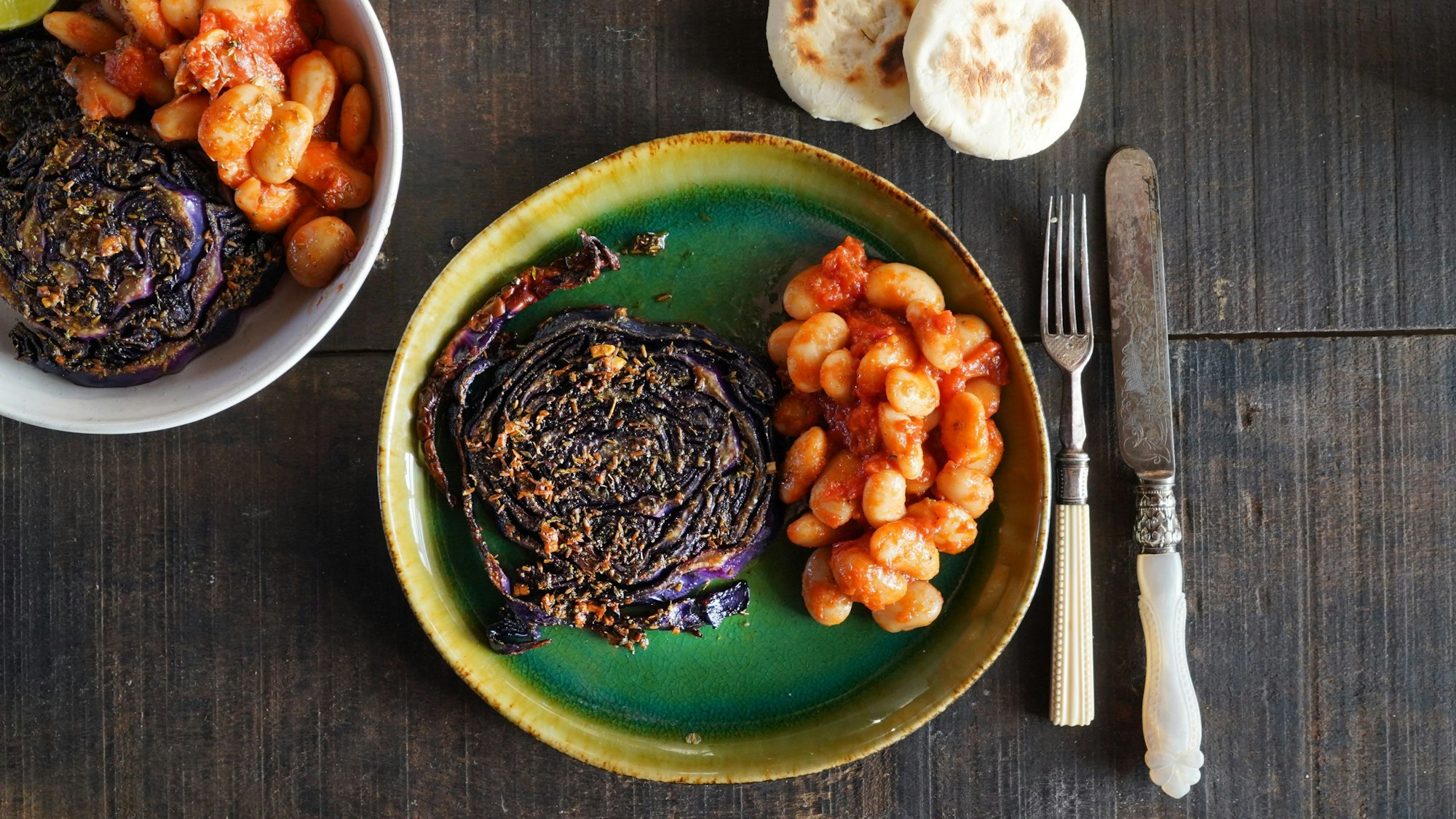 Die geröstete und karamellisierte Rotkohlscheibe liegt neben weißen Bohnen auf einem Teller.