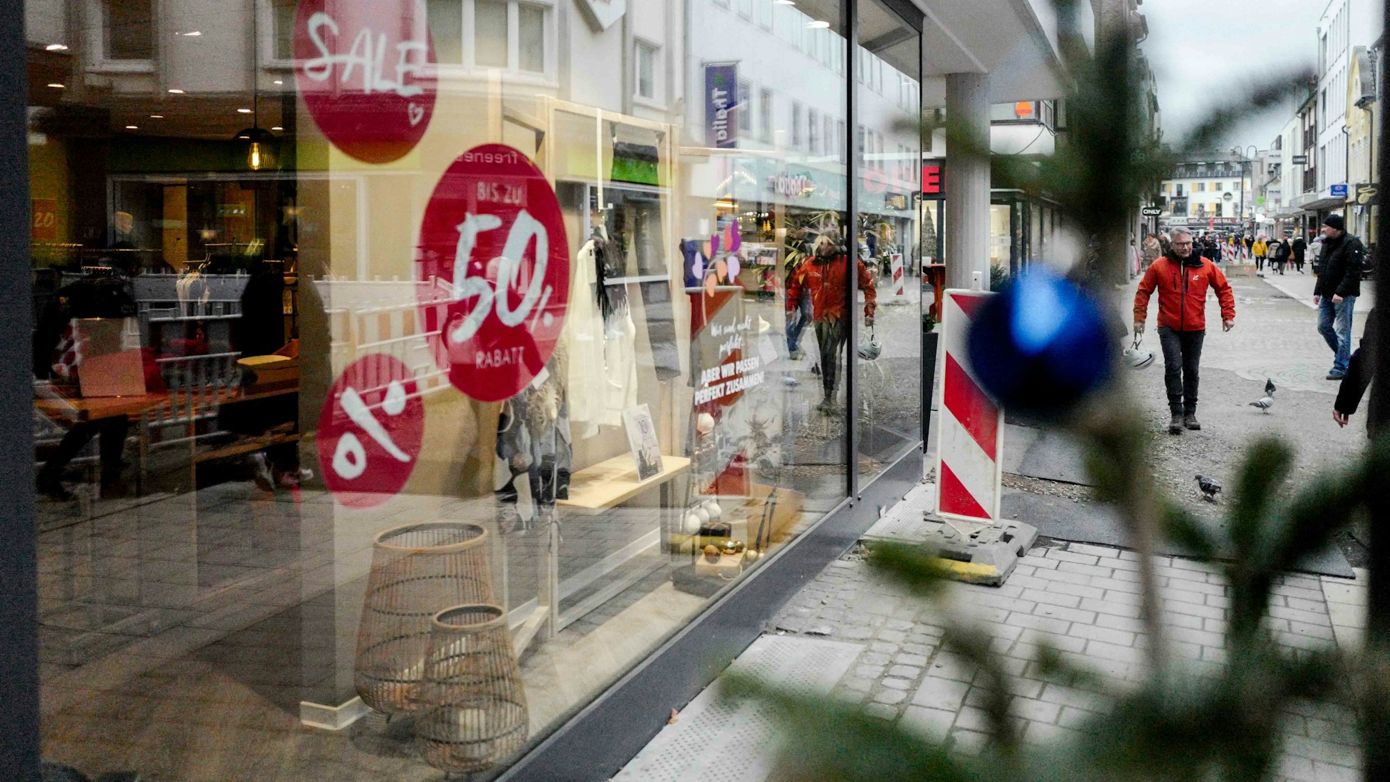 Das Bild zeigt ein Schaufenster in der Euskirchener Innenstadt. Rabatthinweise kleben an der Scheibe, im Vordergrund steht ein Tannenbaum.