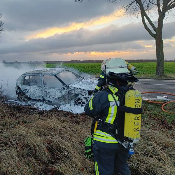 Ein Feuerwehrmann steht vor einem ausgebrannten, qualmenden Auto.