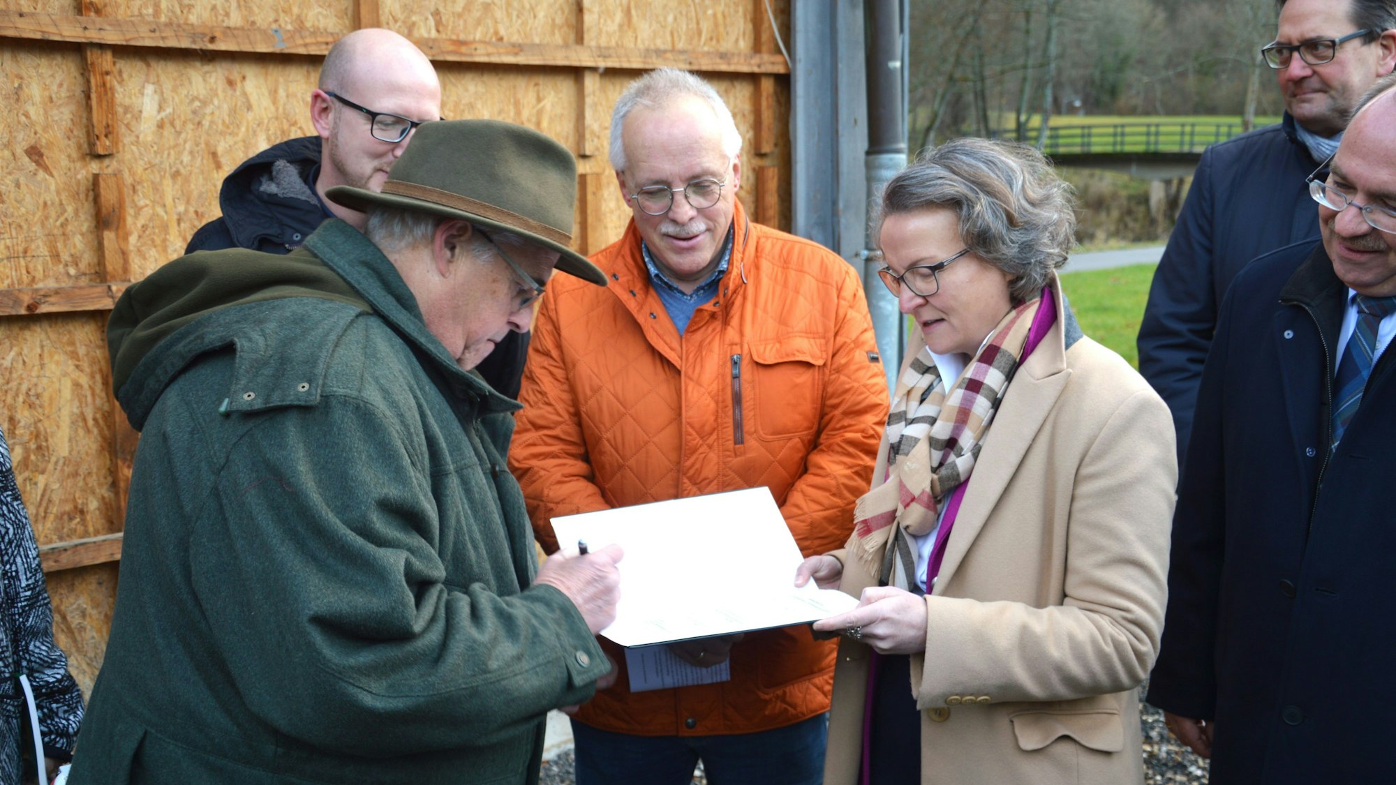 Ditmar Krumpen steht links und unterschreibt den Bescheid. Gegenüber steht die Ministerin für Heimat, Kommunales, Bau und Digitalisierung des Landes Nordrhein-Westfalen Ina Scharrenbach, und Christoph Kammers schaut zu.